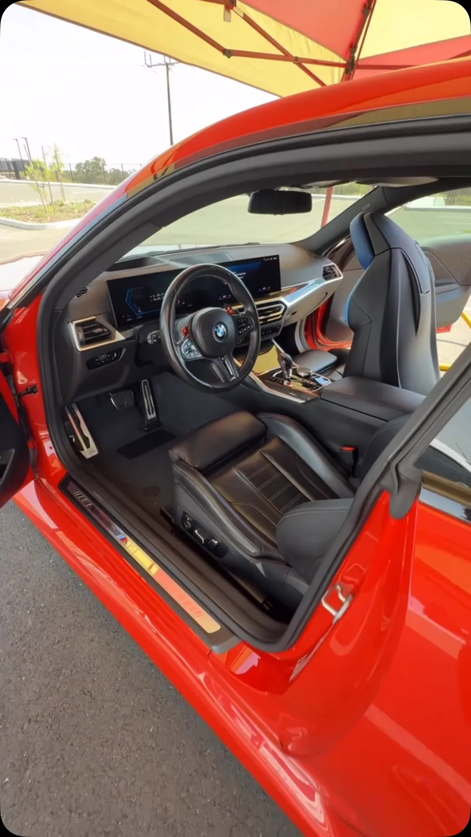 Freshly detailed black leather interior of a red BMW viewed through the open driver door.